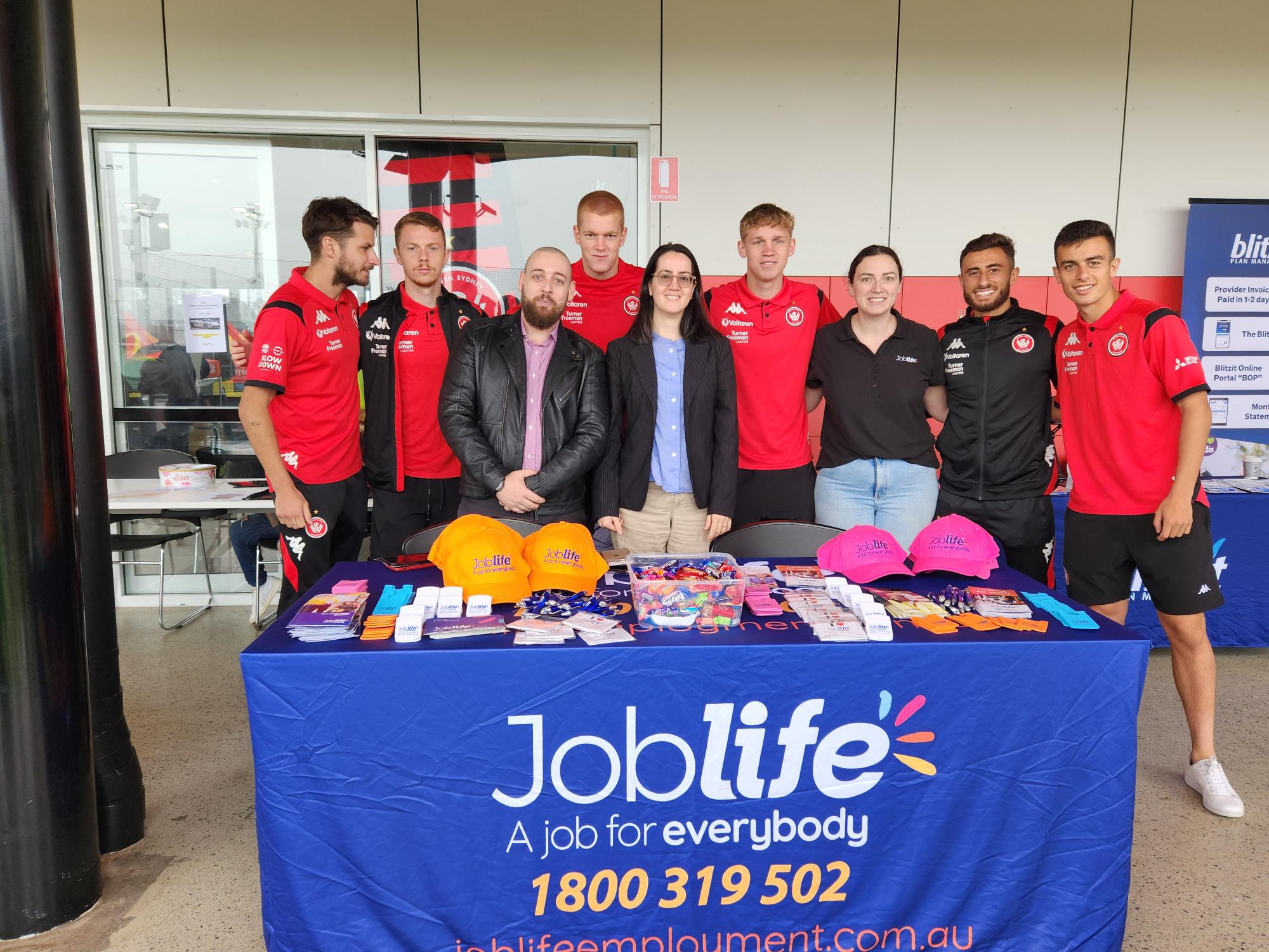 uLaunch - photo of a group of workers dressed in red and black behind a table with 'Joblife' on the banner