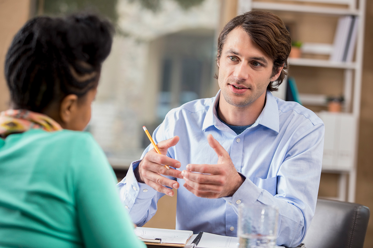 A man and woman talk together. The man is facing towards the camera and we see the woman from behind