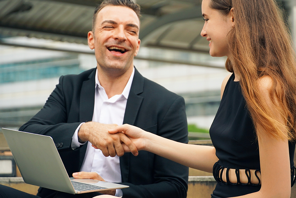 Image of a man shaking hands with a women and smiling. He is working on a laptop