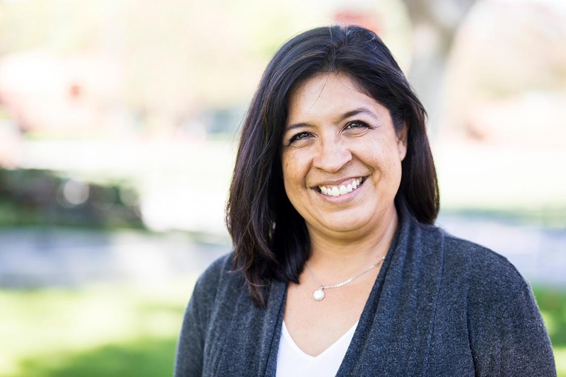 image of a women with dark hair smiling - she is standing outdoors in the sun