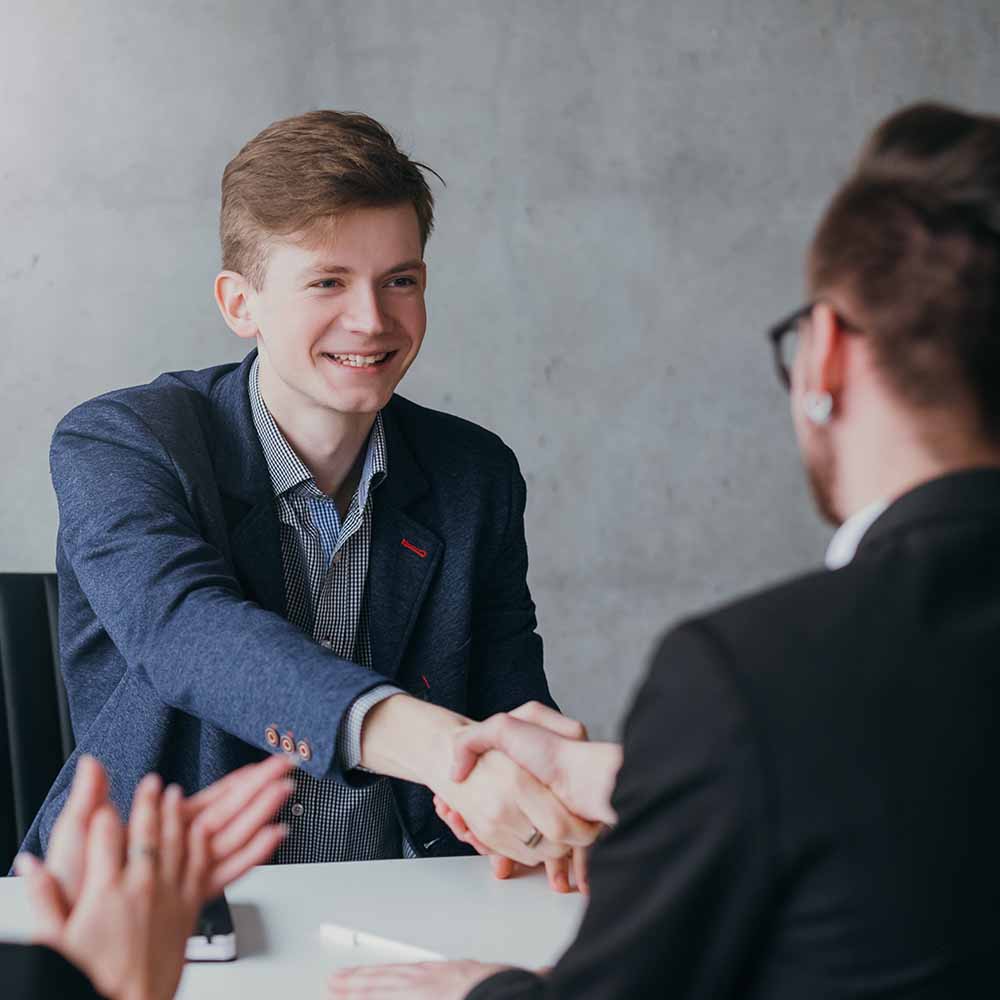 Image of a young man shaking hands with an interviewer. It looks like things have gone well.