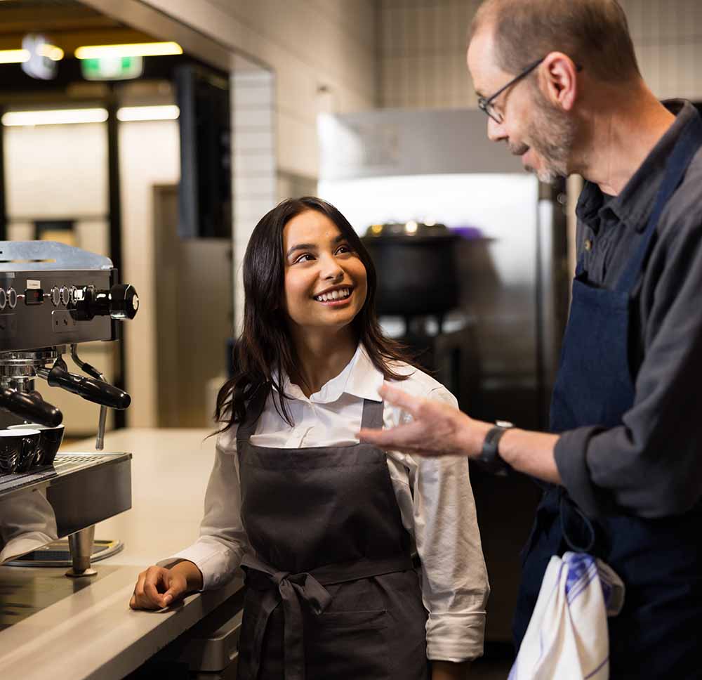 Two cafe workers making coffee - one is getting training from the other