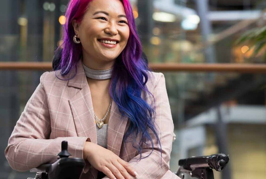 A woman with pink and purple hair sits in a motorised wheelchair.