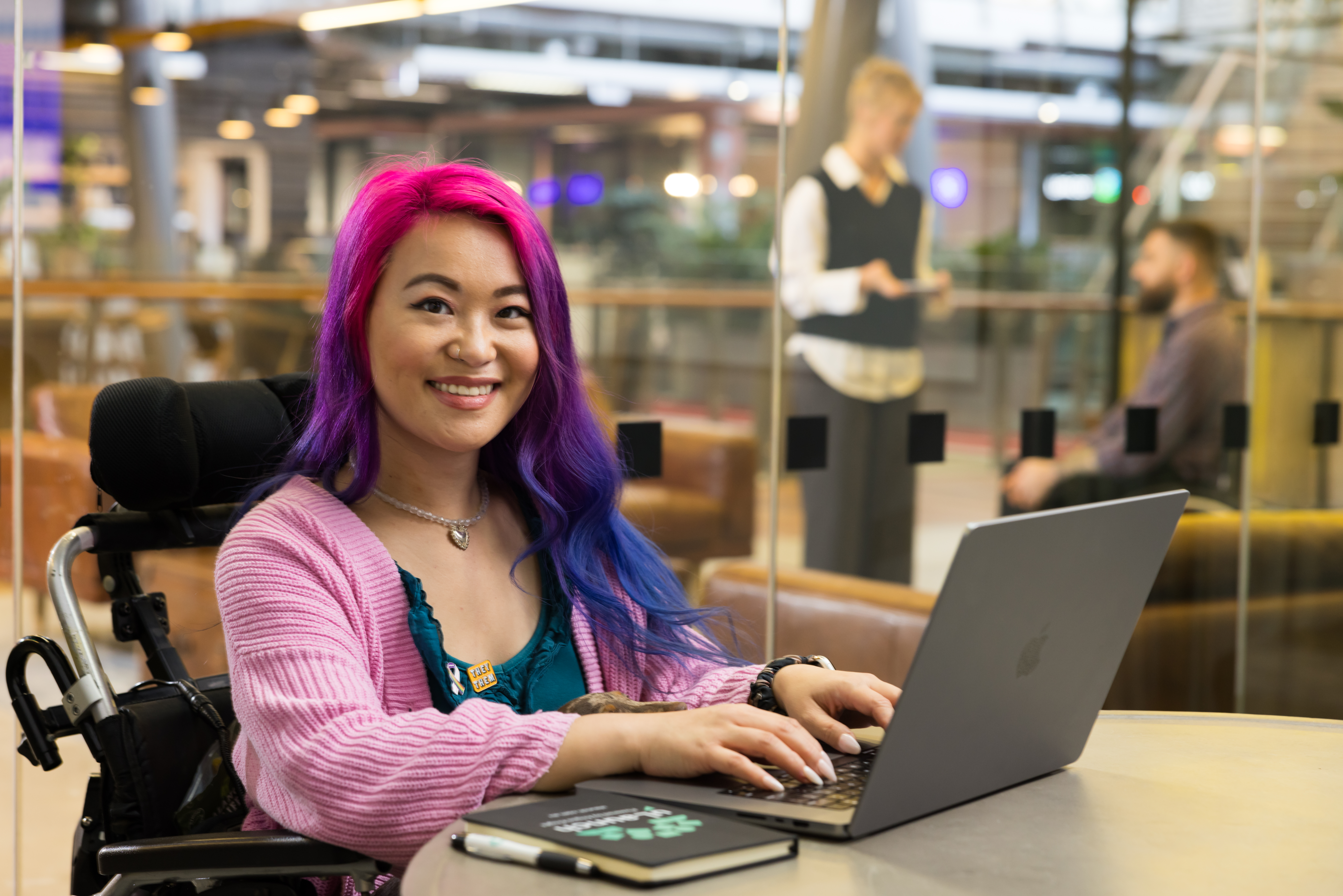 Lady in a wheel chair using a laptop and smiling towards the camera.