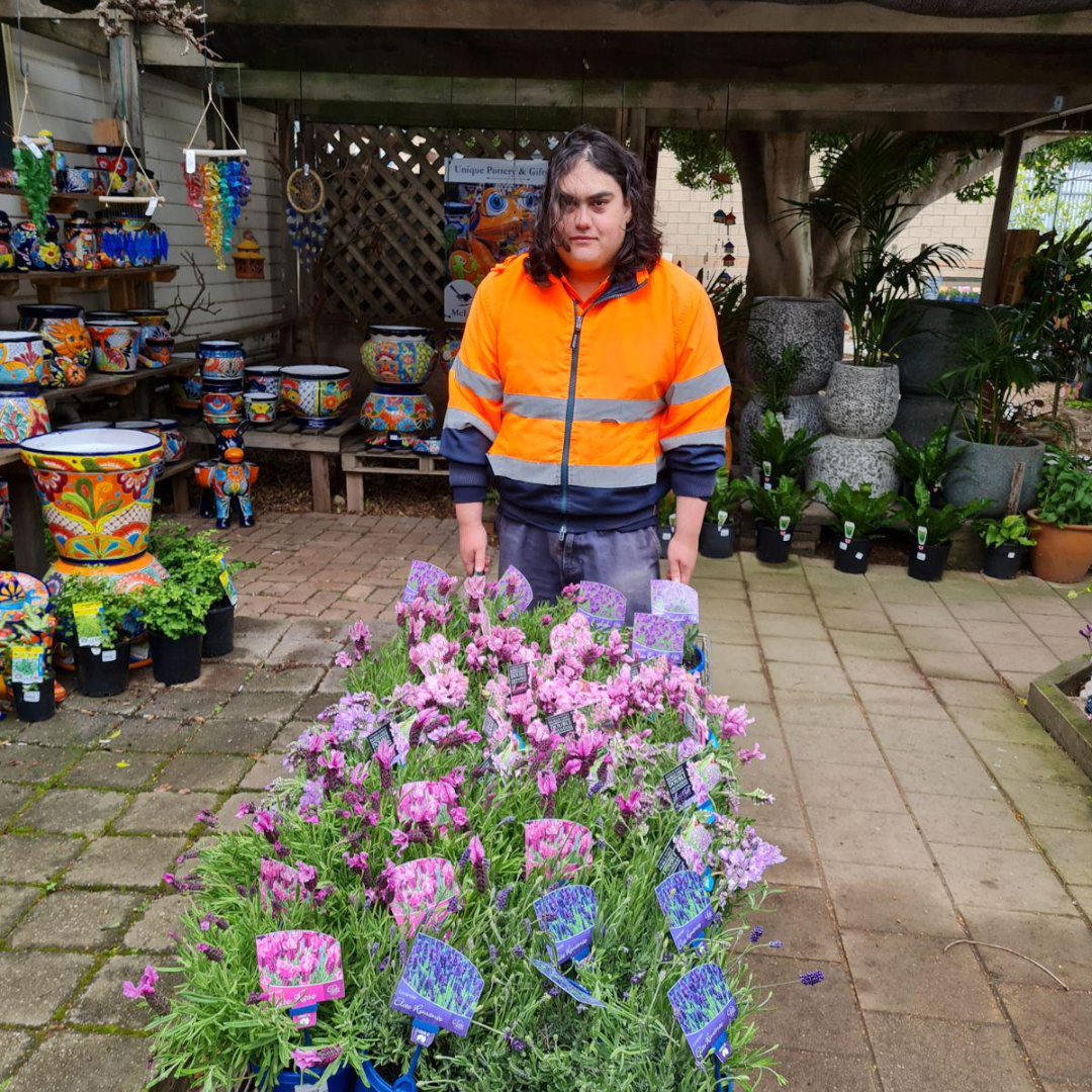 Luke standing beside flowers at his work experience at the garden centre
