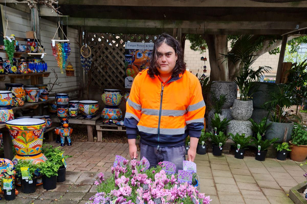 Luke standing beside flowers at his work experience at the garden centre